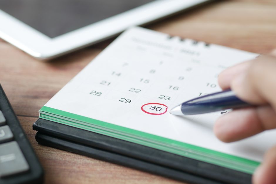 Hand circling an overdue date on a desk calendar with a pen