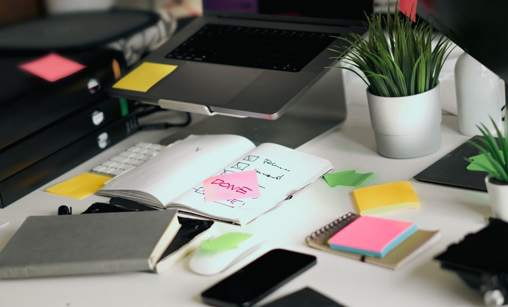 Cluttered desk with laptop, phone, notebook, and sticky notes