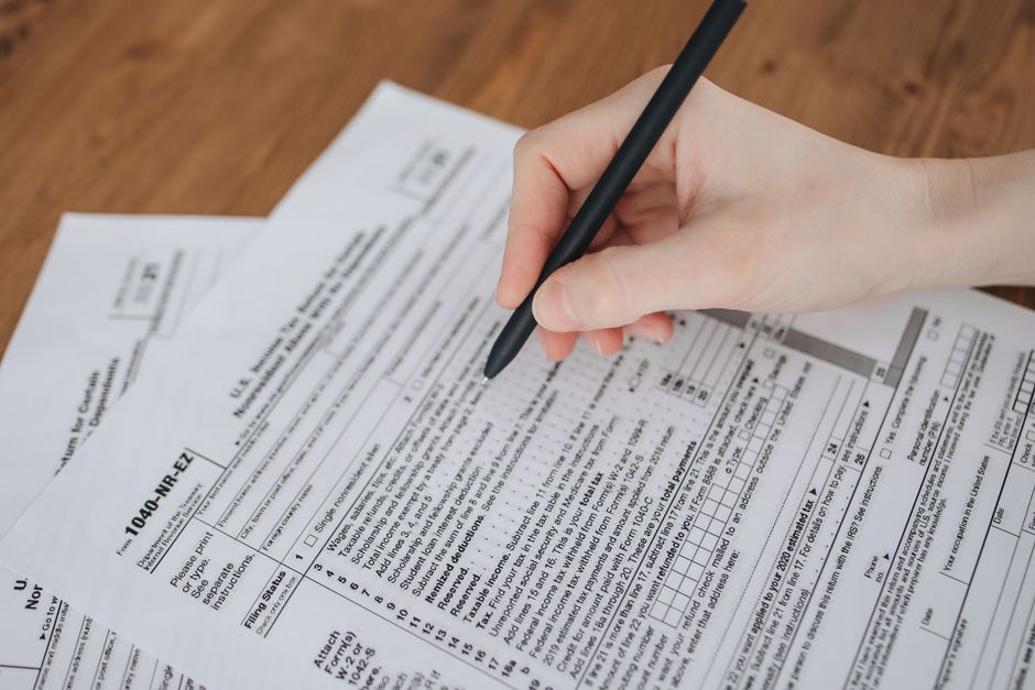 A hand filling out a dense multi-field paper tax form with a pen