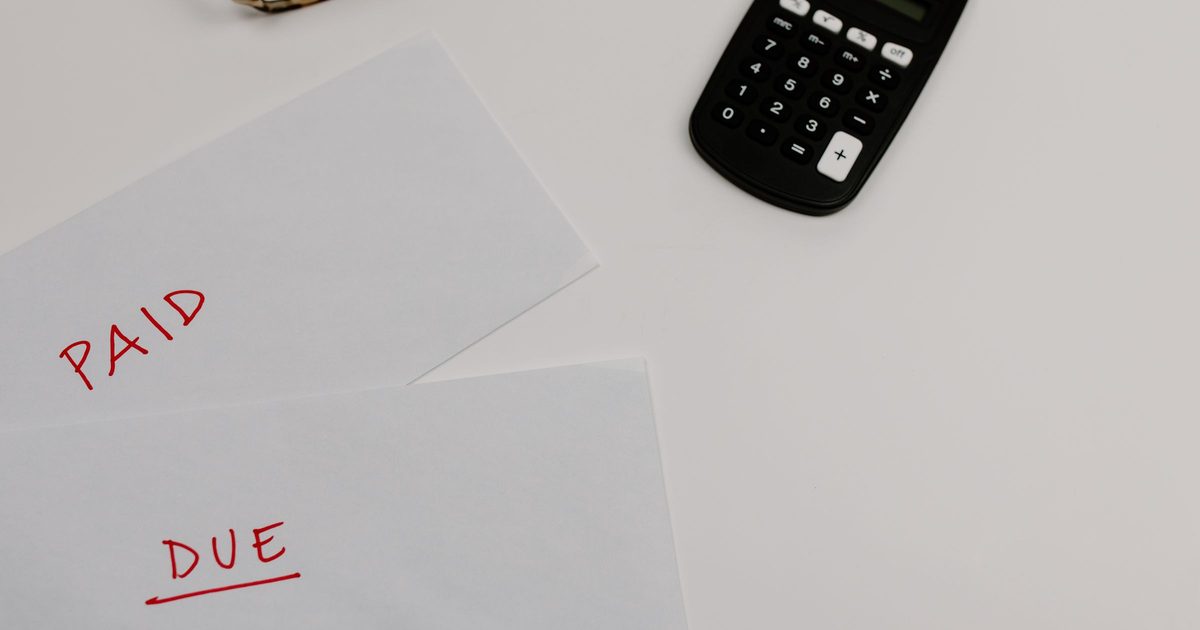 Two sheets of paper on a white desk, one marked PAID and one marked DUE in red pen, beside a calculator