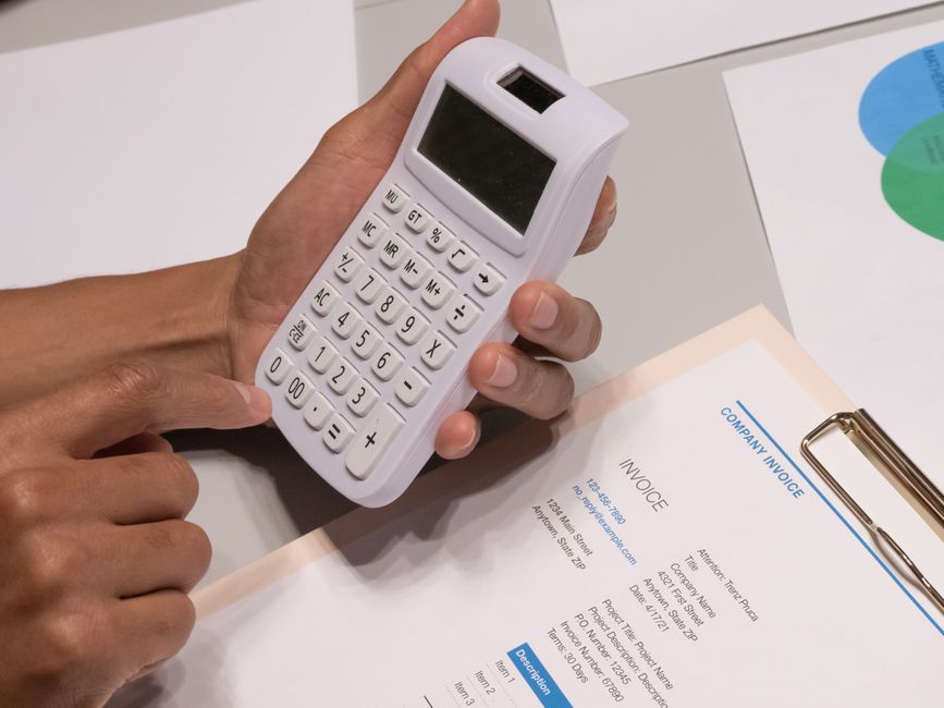 Hand holding a calculator over a printed company invoice