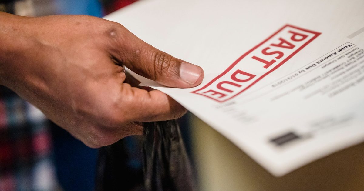 A hand holding a printed bill stamped PAST DUE in large red letters